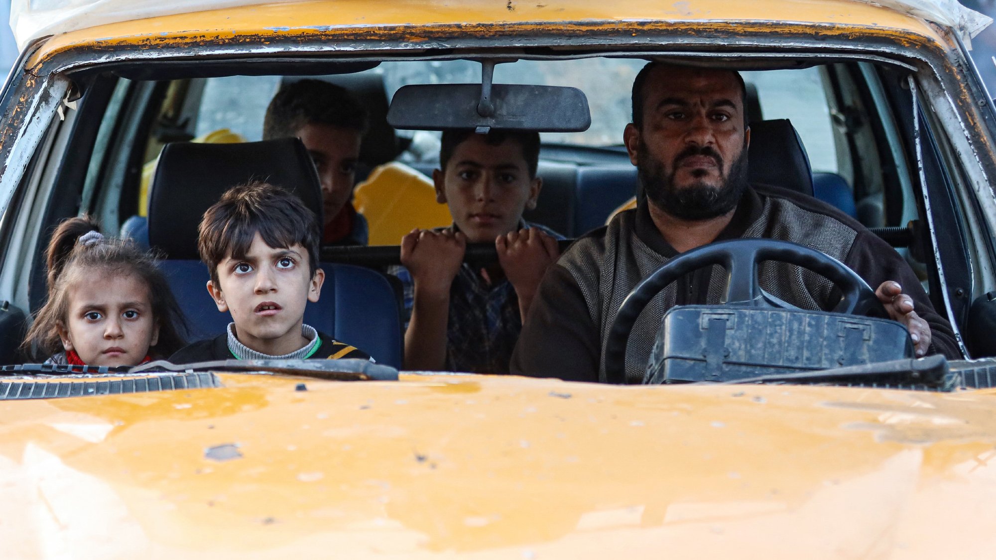 Un homme conduit une vieille voiture avec des enfants inquiets à l'intérieur.
