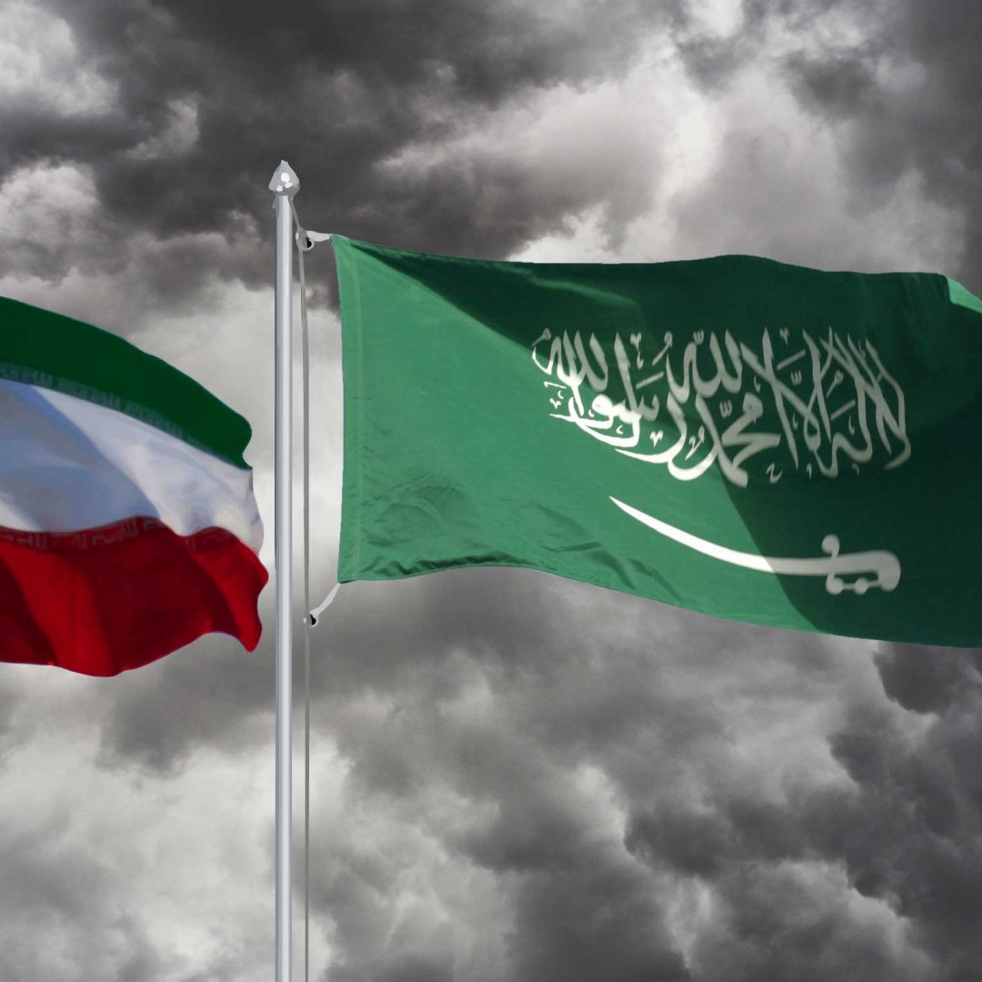 در تصویر، دو پرچم به نمایش درآمده‌اند. پرچم چپ، پرچم ایران است که شامل رنگ‌های سبز، سفید و قرمز به صورت افقی و نشان هشت‌پر در وسط آن است. پرچم راست، پرچم عربستان سعودی است که رنگ اصلی آن سبز تیره است و در وسط آن نوشته عربی به رنگ سفید وجود دارد. زمینه تصویر ابری و طوفانی به نظر می‌رسد که حسی از تنش و درگیری را منتقل می‌کند.