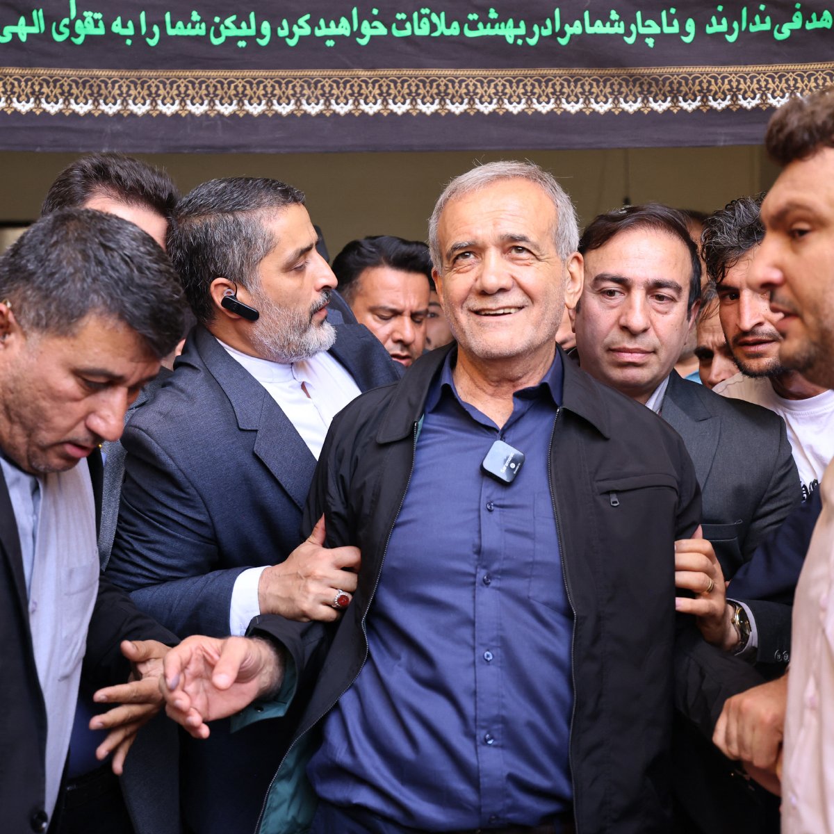 در این تصویر، گروهی از مردان در یک محیط اجتماعی دور یک مرد میانسال جمع شده‌اند. این مرد لبخند بر لب دارد و به نظر می‌رسد در حال برقراری ارتباط با دیگران است. محیط تصویر نشان‌دهنده‌ی یک رویداد مهم یا تجمع است. مردان اطراف او به نظر می‌رسند که به او احترام گذاشته و از او حمایت می‌کنند. متن در بالای تصویر به زبان فارسی نوشته شده است و به نظر می‌رسد حاوی یک پیام یا عنوان خاص باشد.