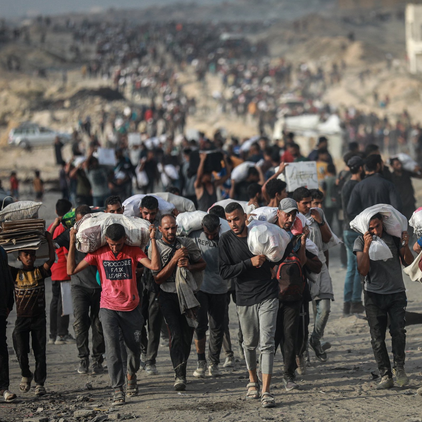 Un grupo de personas camina por un terreno árido, llevando sacos y luciendo cansados.