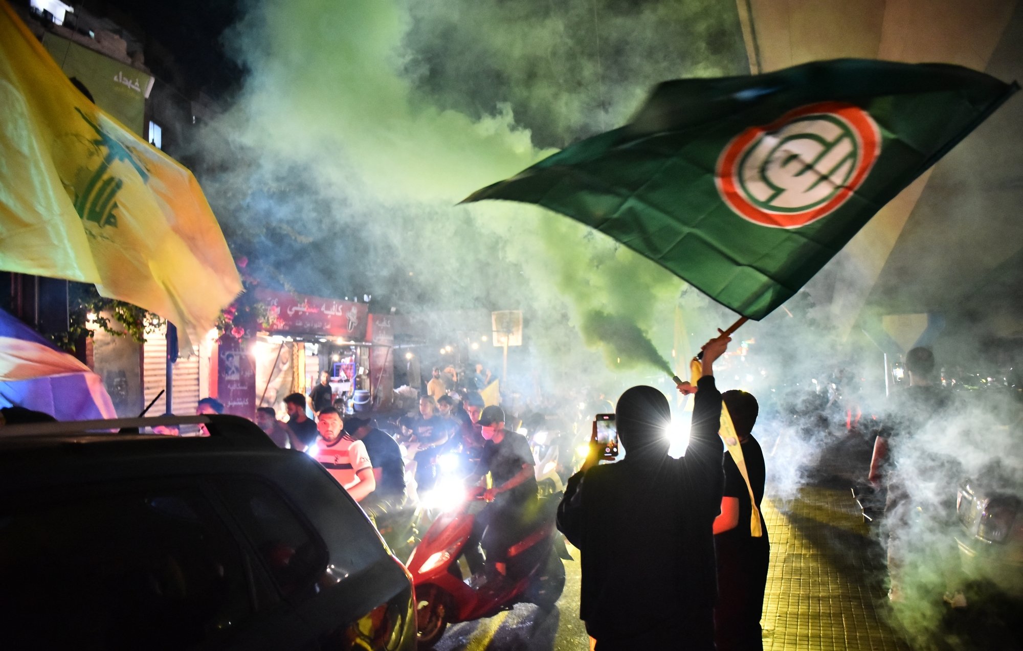 Des manifestants brandissent des drapeaux sous une fumée colorée dans une ambiance festive.