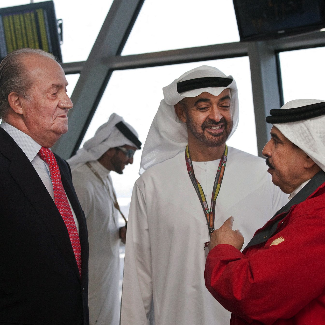 في الصورة، يظهر ثلاثة رجال يتحدثون معًا. يرتدي أحدهم بدلة رسمية، بينما يرتدي الآخرون الملابس التقليدية العربية. الخلفية تحتوي على شاشات عرض لمعلومات الطيران. يبدو أن الحديث يجري في مكان رسمي، مثل مطار أو مركز اجتماعات. الجو العام يوحي بالتقارب والتفاعل الودي بين الأشخاص.