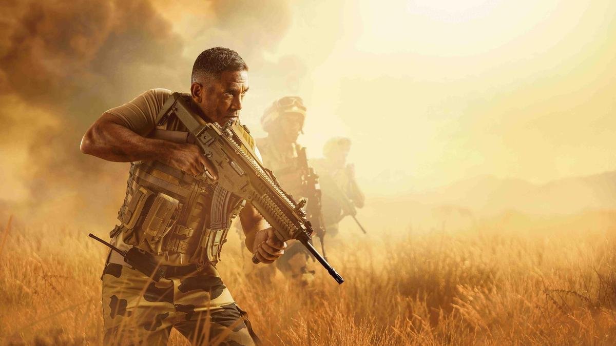 تظهر الصورة مشهدًا عسكريًا في بيئة صحراوية أو مفتوحة. يُرى في المقدمة رجل يرتدي زيًا عسكريًا ويحمل سلاحًا، يبدو مركزًا وجادًا. في الخلفية، يظهر عدد من الجنود الآخرين يتقدمون معه، مما يعزز الإحساس بالتعاون والعمل الجماعي. السماء تمتزج بألوان دافئة، مما يضيف جوًا من التوتر والحركة.