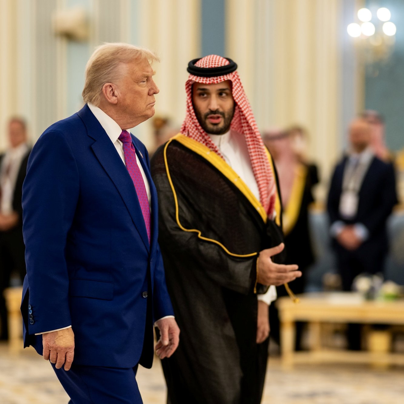 Deux hommes en costume, l'un américain et l'autre saoudien, discutent dans un hall élégant.