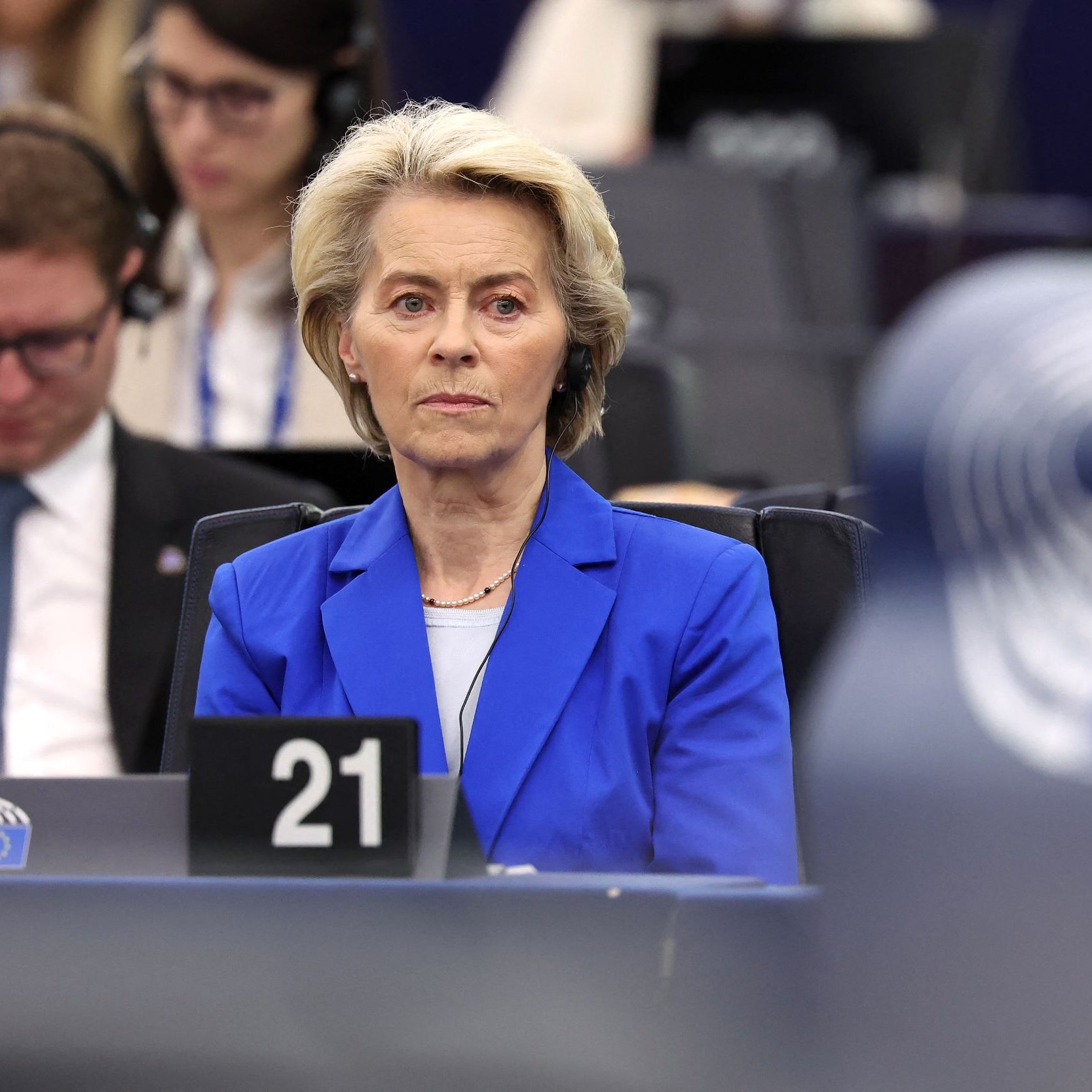 L'image montre une femme assise dans un environnement de réunion, probablement au sein d'une institution européenne, comme le Parlement européen. Elle porte un blazer bleu et semble concentrée sur un sujet abordé lors de la séance. En arrière-plan, on aperçoit d'autres personnes, également attentives. L'atmosphère paraît formelle et sérieuse, et des équipements audio sont visibles, suggérant une translation ou un écoute attentive des débats.