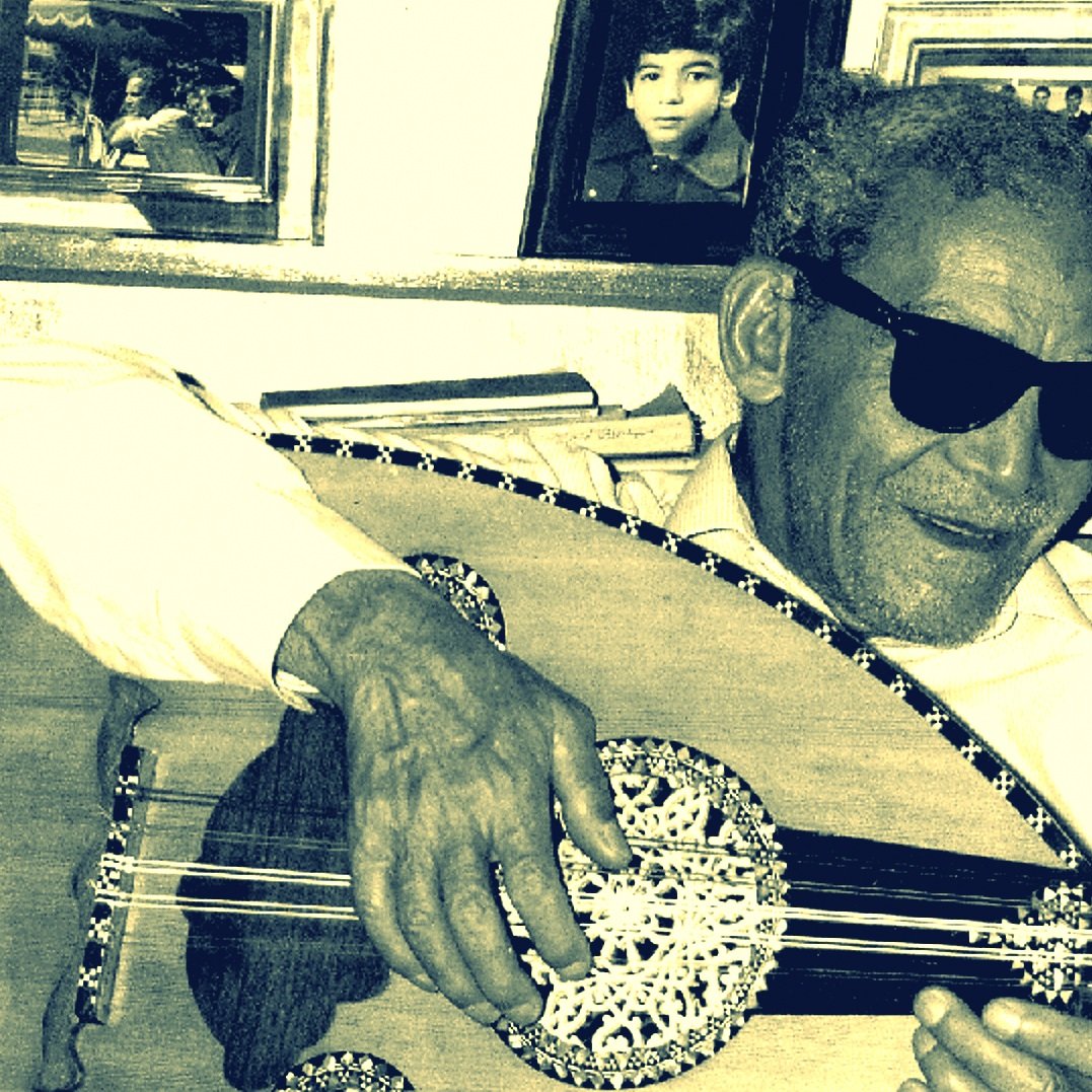 الصورة تظهر رجلًا مسنًا يرتدي نظارات شمسية ويعزف على آلة العود. يبدو سعيدًا ومسترخيًا، محاطًا بإطارات صور على الجدار خلفه. الأسلوب الذي يقدّم به العزف يعكس شغفه بالموسيقى. الأجواء تدل على لمسة من الح nostalgia، مع تفاصيل تعكس العناية والحنين إلى الماضي.