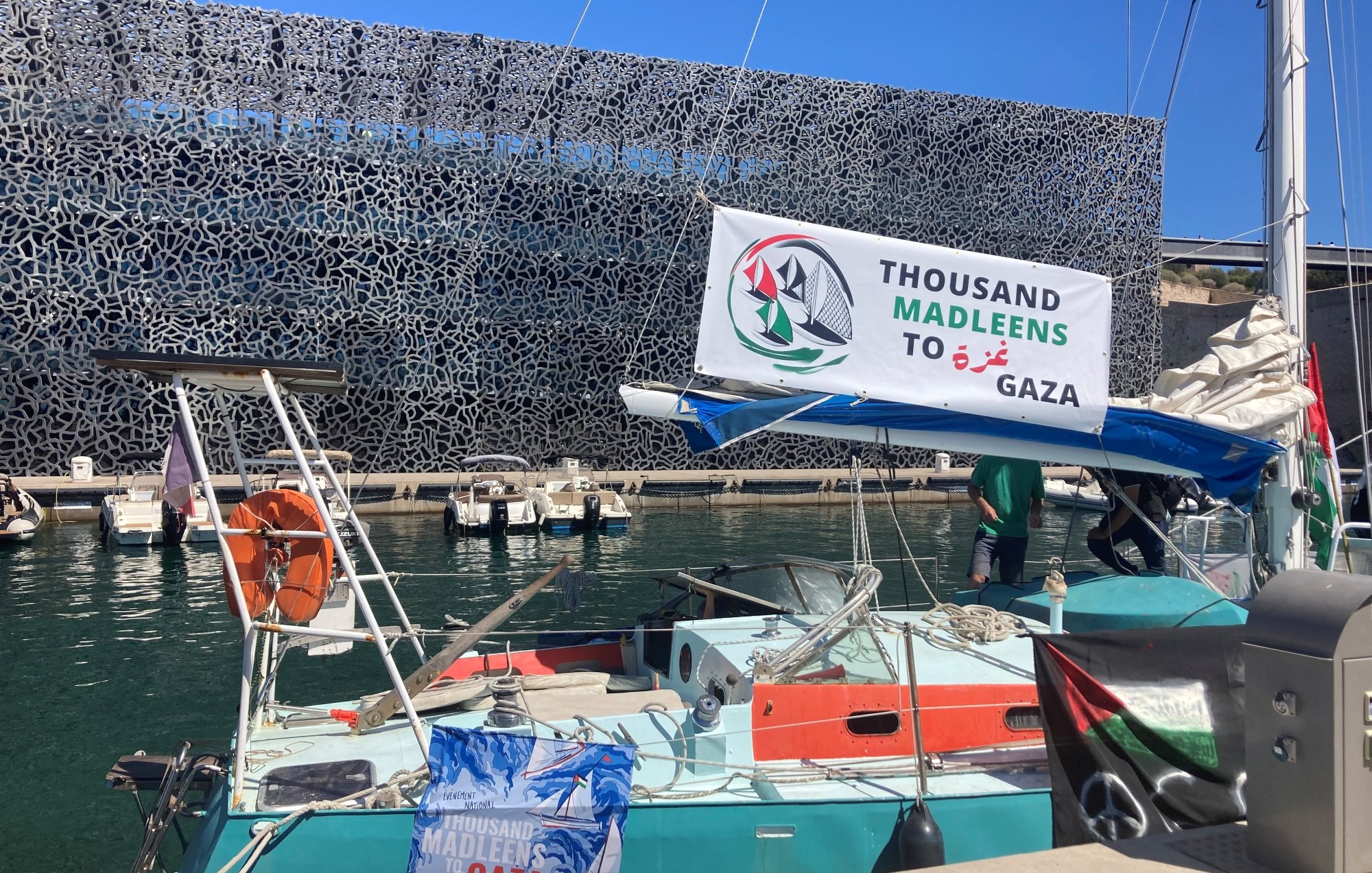 Una barca in un porto con un banner che supporta Gaza e un fondale moderno.
