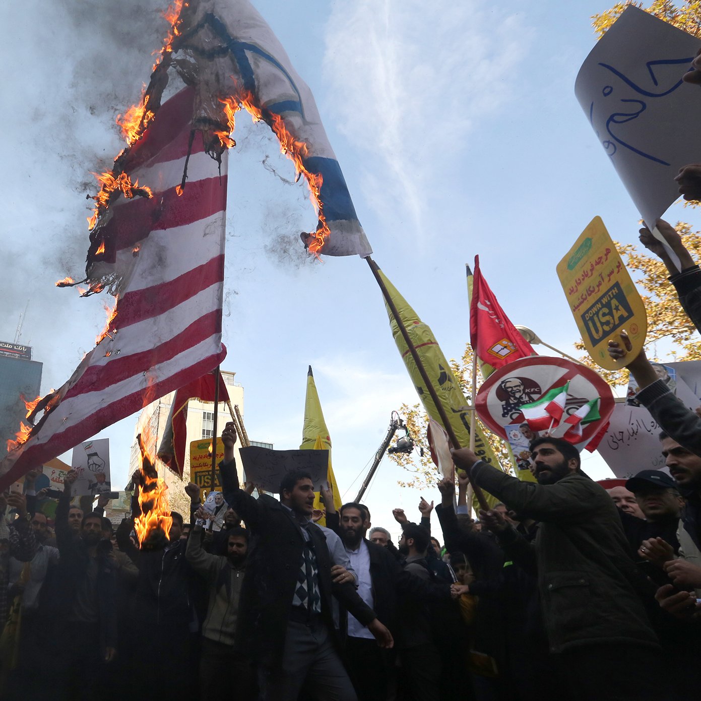 در این تصویر، جمعیتی در حال برگزاری یک تظاهرات هستند. گروهی از افراد در حال آتش زدن پرچم‌هایی با نمادهای مشخص هستند. پشت زمینه تظاهرات، ساختمان‌ها و تابلوهای تبلیغاتی دیده می‌شود. شمار زیادی از تظاهرکنندگان در دست خود پلاکاردهایی نشان می‌دهند که بر روی آن‌ها شعارهایی نوشته شده است. جو عمومی تصویر نشان‌دهندهٔ هیجان و احساسات قوی شرکت‌کنندگان است.