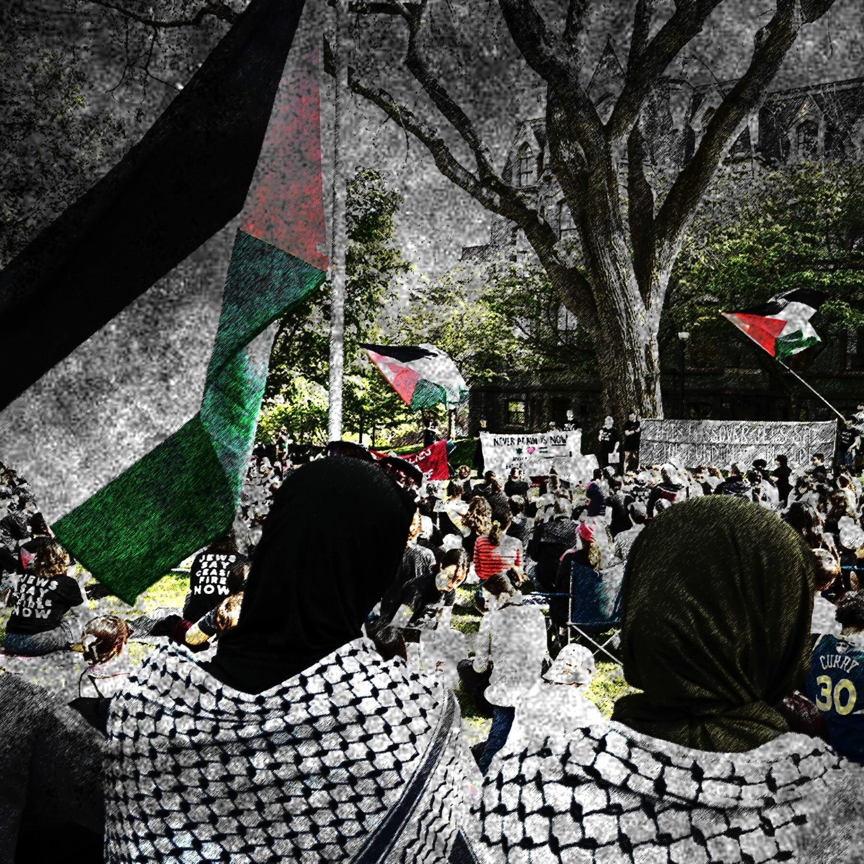 L'immagine mostra una manifestazione in cui partecipano molte persone, alcune delle quali indossano sciarpe tradizionali palestinesi. Si possono vedere delle bandiere palestinesi sventolare sullo sfondo. La scena è caratterizzata da una grande affluenza di partecipanti, con un'atmosfera di attivismo e solidarietà. Gli alberi e l'architettura circostante forniscono un contesto urbano alla manifestazione, suggerendo un forte impegno per una causa sociale.