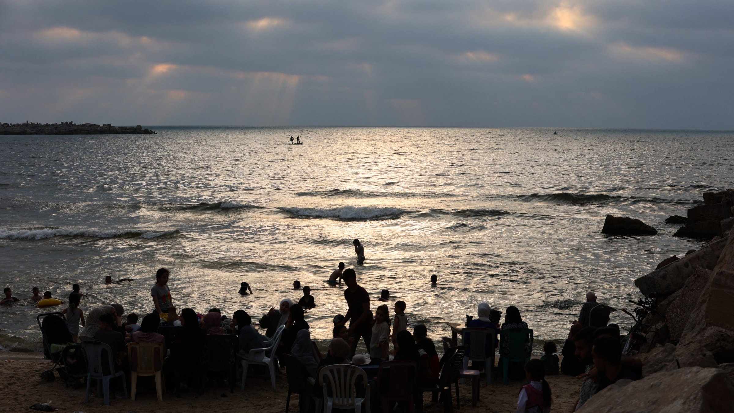 Plage animée au crépuscule, avec des gens dans l'eau et sur le sable.