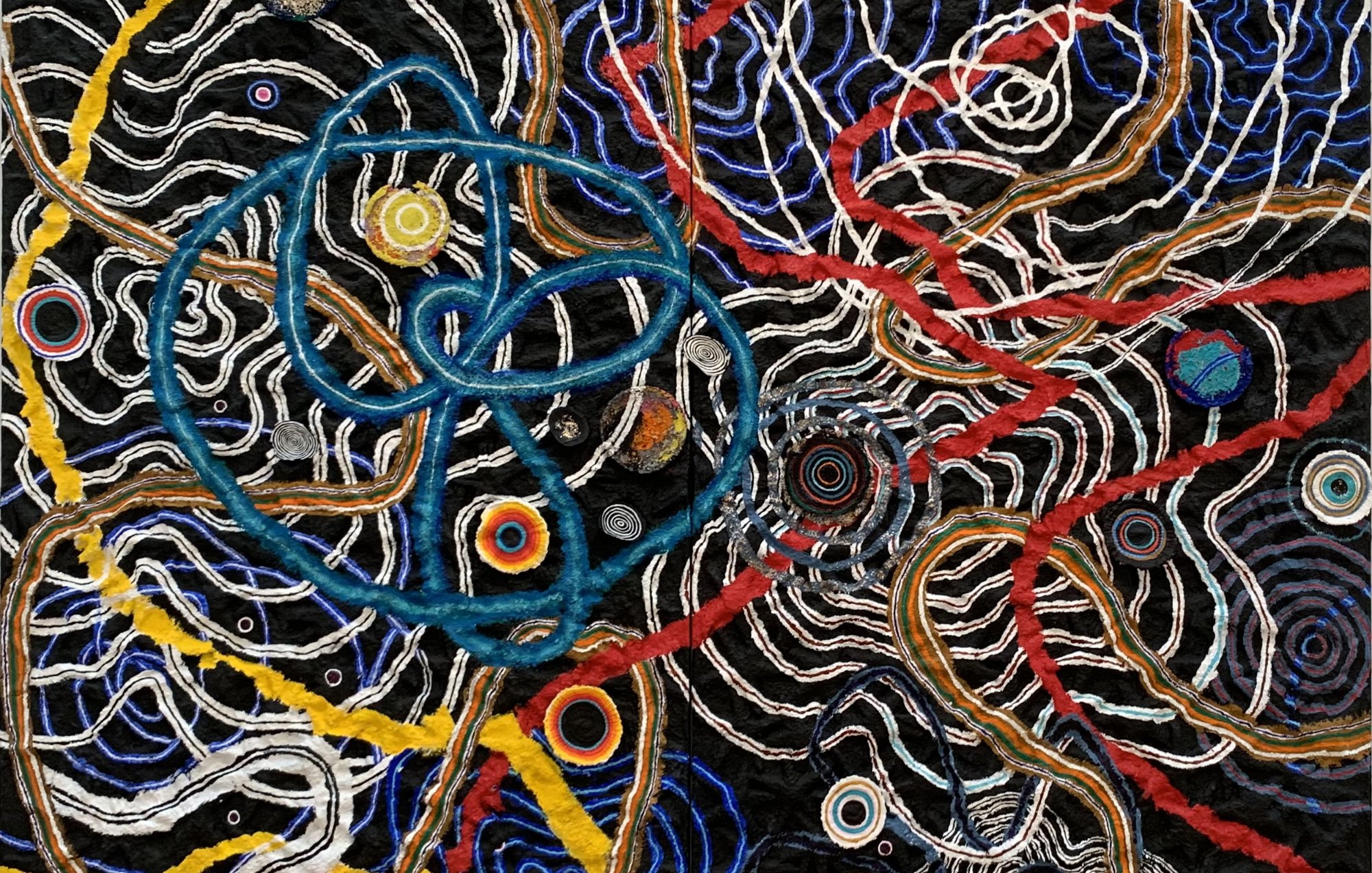 The image features a vibrant abstract design with intertwining lines and shapes. It includes a variety of colors, such as blue, red, yellow, and white, creating a dynamic and complex pattern. The background is dark, which enhances the brightness of the interwoven elements. Circular forms are scattered throughout, contributing to the overall sense of movement and depth, resembling a blend of organic and geometric motifs. The texture suggests a tactile quality, inviting viewers to explore the intricate connections within the composition.
