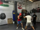 Deux boxeurs s'entraînent dans une salle avec des sacs de frappe et un entraîneur.