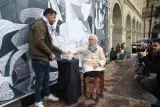 Un homme tend un objet à une vieille dame assise, lors d'un événement public extérieur.