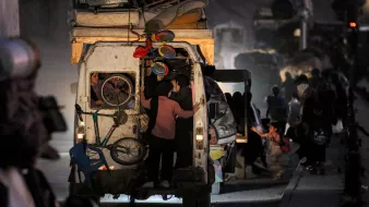 Un furgone pieno di oggetti, persone in movimento in un ambiente polveroso e notturno.