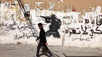 Un garçon marche devant un mur graffiti avec une silhouette de soldat.