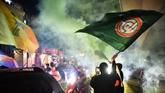 Des manifestants brandissent des drapeaux sous une fumée colorée dans une ambiance festive.