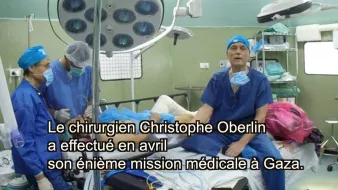 L'image montre une scène dans une salle d'opération. On y voit plusieurs professionnels de la santé en train de travailler. Ils portent des blouses et des masques de protection caractéristiques des environnements médicaux. Au centre, un patient est couché sur une table d'opération, tandis qu'un chirurgien, probablement Christophe Oberlin, s'adresse à la caméra. Des équipements médicaux, tels que des lampes et des instruments chirurgicaux, sont visibles dans la pièce. Le texte indique que cette intervention a eu lieu en avril lors d'une mission médicale à Gaza.