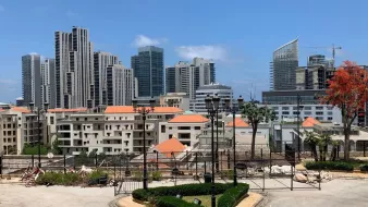 صورة لمدينة حديثة، مباني مرتفعة، سماء زرقاء وأشجار. يبدو النشاط العمراني واضحًا.