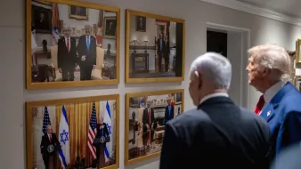 Des hommes politiques regardent des photos accrochées au mur, représentant des rencontres officielles.