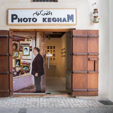 Une porte en bois s'ouvre sur une galerie photo avec des images exposées.