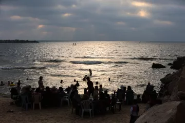 Plage animée au crépuscule, avec des gens dans l'eau et sur le sable.