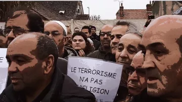 L'image montre un groupe de personnes rassemblées lors d'une manifestation. Ils semblent préoccupés et écoutent attentivement, avec des expressions sérieuses. Certains tiennent des pancartes, dont une qui porte le message "LE TERRORISME N'A PAS DE RELIGION". L'environnement semble urbain, avec des bâtiments en arrière-plan. L'atmosphère suggère une revendication ou une protestation sur un sujet important.