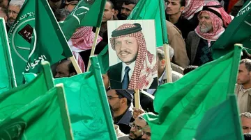 L'image montre une foule rassemblée, tenant des drapeaux verts. Au centre, il y a un portrait d'un homme, probablement une figure importante, qui est mis en avant parmi les drapeaux. L'atmosphère semble être celle d'une manifestation ou d'un rassemblement politique, avec des participants engagés et un message de soutien collectif.