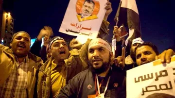 L'image montre un groupe de manifestants engagés dans une démonstration. Ils tiennent des pancartes et des drapeaux, exprimant visiblement leurs opinions politiques. Les visages des participants montrent des émotions intenses, allant de la passion à la détermination. Les slogans et les portraits visibles sur les affiches semblent se rapporter à un leader ou une figure politique, témoignent d'un moment de mobilisation collective. L'ambiance est dynamique, évoquant un fort sentiment de communauté et d'engagement.