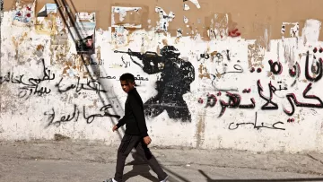 Un garçon marche devant un mur graffiti avec une silhouette de soldat.