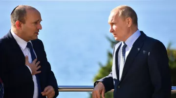 L'image montre deux hommes en discussion près d'une balustrade, avec une vue sur la mer en arrière-plan. L'un d'eux, portant une kippa, semble s'exprimer avec gestuelle, tandis que l'autre écoute attentivement. Les deux hommes sont habillés de manière formelle, et l'atmosphère paraît concentrée. La lumière du jour éclaire la scène, suggérant un cadre extérieur agréable.