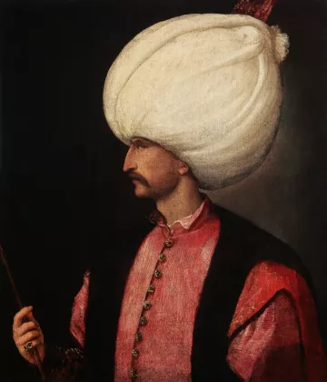 L'image représente un homme en profil, portant un turban blanc imposant. Il est habillé d'une tunique rose ornée de boutons et d'un veston noir, ce qui lui donne un aspect richement décoré. Son visage est finement dessiné, mettant en valeur sa moustache. Il tient un bâton dans une main, ce qui suggère une position de pouvoir ou d'autorité. L'arrière-plan est sombre, ce qui fait ressortir les détails de sa tenue et de son expression.