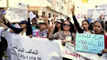 L'image montre un groupe de femmes participant à une manifestation. Elles tiennent des banderoles et des pancartes, exprimant des revendications liées aux droits des femmes. Certaines d'entre elles lèvent les mains en faisant le signe de la victoire. L'ambiance semble engagée et déterminée, avec des expressions de solidarité parmi les participantes.