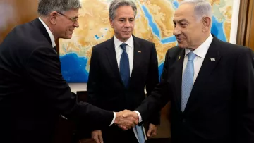 L'image montre trois hommes dans un cadre formel. À gauche, un homme tend la main pour saluer un autre homme à droite, qui semble être le Premier ministre israélien. Au centre, un homme observe la scène. Le fond présente une carte de la région méditerranéenne, ce qui suggère un contexte diplomatique ou de négociations. Les hommes sont habillés de façon professionnelle, ce qui renforce l'atmosphère sérieuse de la rencontre.