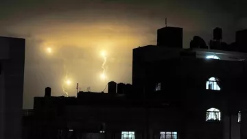 L'image montre un ciel nocturne illuminé par des éclairs, avec des nuages sombres en arrière-plan. On peut voir des bâtiments en silhouette, avec des fenêtres lumineuses qui créent un contraste avec l'obscurité environnante. Les éclairs apparaissent comme des points lumineux dans le ciel, ajoutant une atmosphère dramatique à la scène.