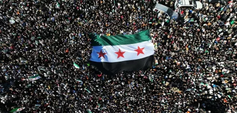 Une foule dense brandit un grand drapeau noir, blanc et vert avec trois étoiles rouges.