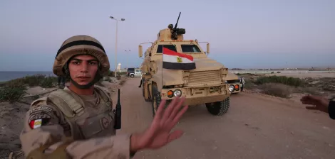 A soldier in uniform gestures as an armored vehicle marked with the Egyptian flag approaches.
