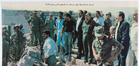 A group of military personnel and civilians gathers at a rubble site, surveying damage.