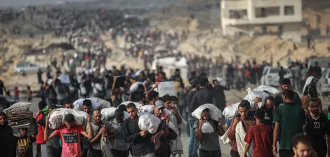 Un grupo de personas camina por un terreno árido, llevando sacos y luciendo cansados.