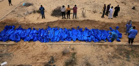 Des corps enveloppés de bleu sont placés dans une fosse, entourés de personnes en deuil.