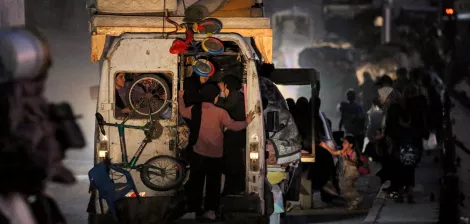 Un furgone pieno di oggetti, persone in movimento in un ambiente polveroso e notturno.