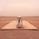 L'image montre une structure isolée située dans un paysage désertique. Au centre, il y a un long bassin en pierre, entouré par une surface plane et aride. Le sol est de couleur beige et semble sec et craquelé, tandis que l'atmosphère est légèrement brumeuse, ce qui donne une impression de chaleur et d'immensité désertique. Au loin, on aperçoit des collines ou des dunes qui se fondent avec le ciel dans une teinte douce et uniforme. L'endroit dégage une sensation de tranquillité et de solitude.