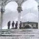 L'image montre une scène en noir et blanc, probablement historique, avec un groupe de soldats se tenant sur des marches devant un édifice. On peut apercevoir un dôme caractéristique au fond, ainsi que des arches en pierre en avant-plan. L'atmosphère est solennelle et le lieu semble chargé d'histoire. Les soldats sont habillés de manière militaire et semblent en position de garde.