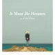 L'image représente une affiche de film intitulée "It Must Be Heaven", réalisé par Elia Suleiman. On y voit un homme de dos, portant un chapeau, se tenant debout sur un rocher au bord de la mer. L'horizon est dégagé, avec un ciel bleu clair. Le titre du film est inscrit en lettres blanches en bas de l'affiche, avec également le nom du réalisateur. L'ensemble de l'image évoque une ambiance contemplative et poétique.