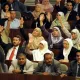 L'image montre un rassemblement dans un espace législatif, probablement au sein d'une assemblée ou d'un parlement. De nombreuses personnes sont présentes, avec une majorité levant la main, ce qui indique probablement un vote ou une approbation. Les participants semblent porter des tenues formelles, et certaines femmes portent le hijab. On observe une diversité de participants, tant en termes de genre que d'âge. L'environnement évoque une atmosphère de discussion et de prise de décision collective.