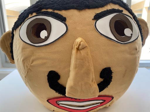 Un grand coussin rond avec un visage amical, nez proéminent et moustache noire.