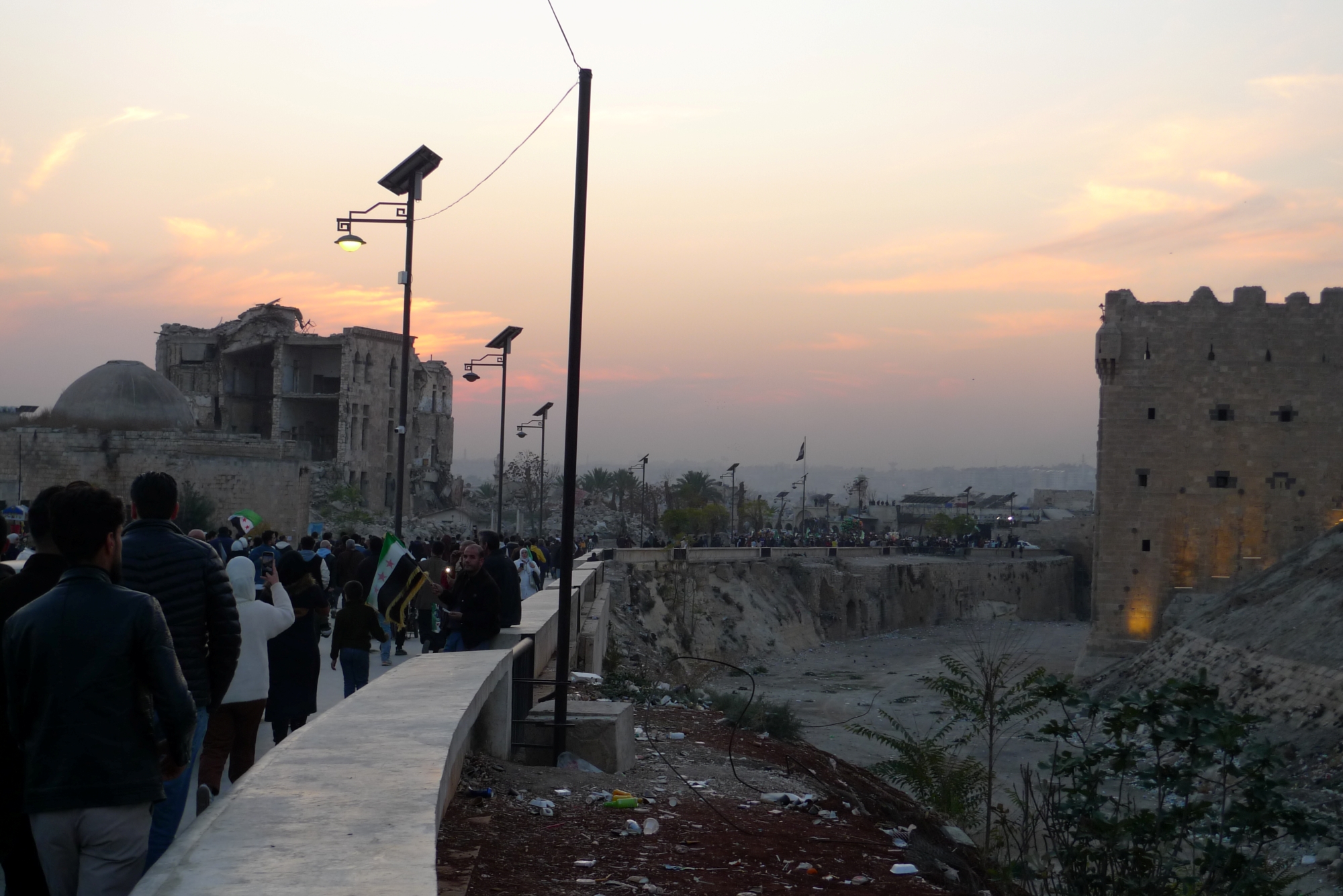 Ruines historiques au coucher du soleil, avec une foule le long d'un chemin.
