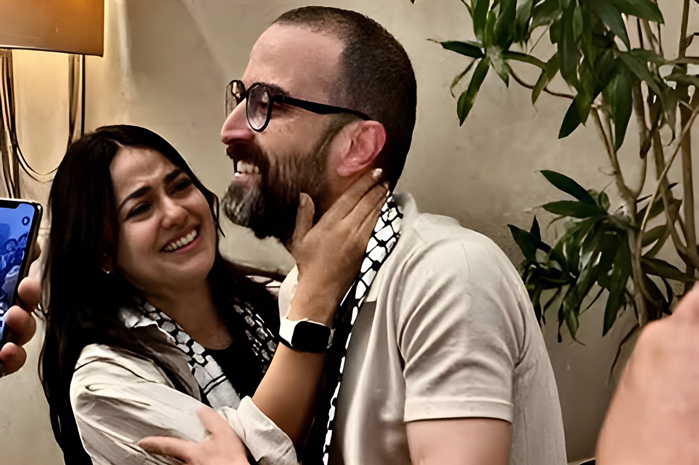 Due persone si abbracciano sorridendo, circondate da piante e un'atmosfera amichevole.