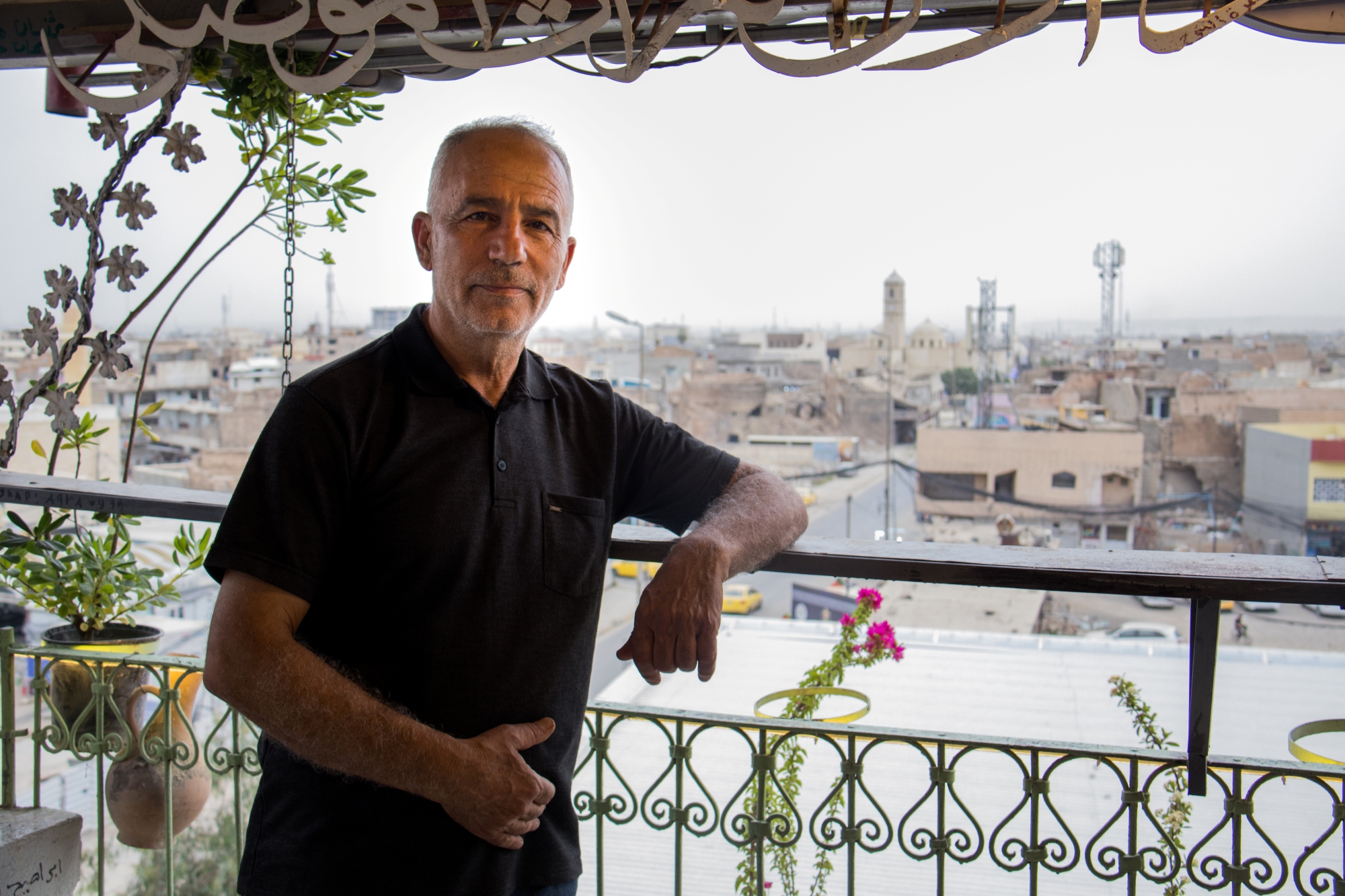 Un homme souriant se tient sur un balcon avec une vue sur une ville.
