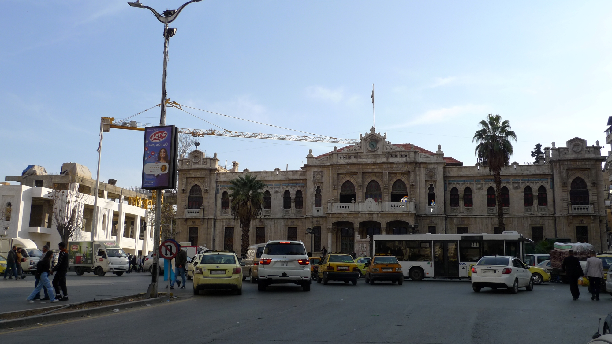 Des voitures au premier plan, un grand bâtiment ancien de style architectural, ciel bleu.