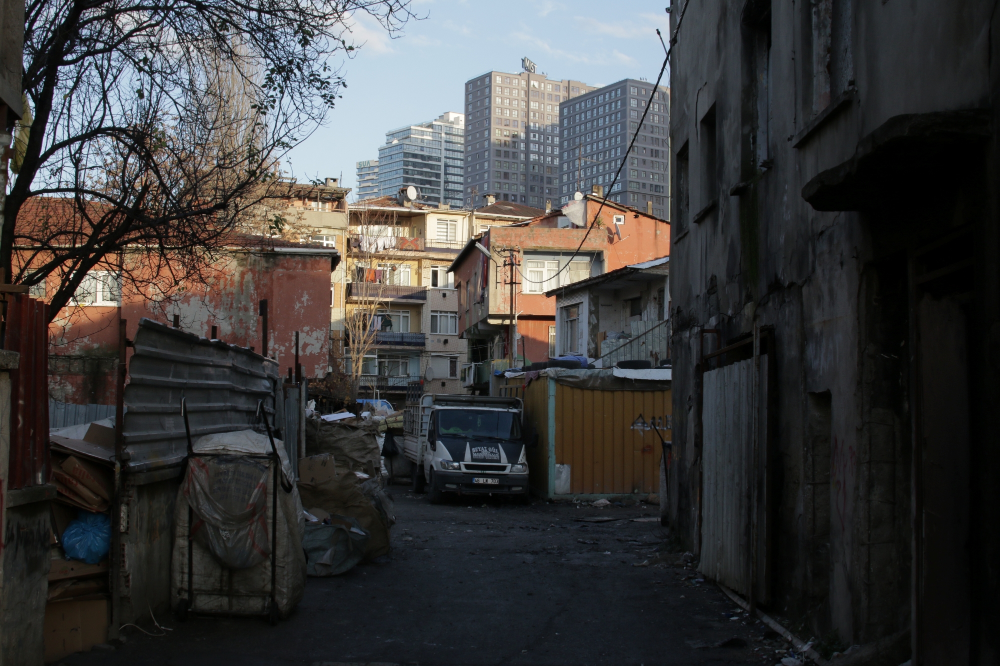 Allée étroite avec bâtiments délabrés et gratte-ciel en arrière-plan. Ambiance urbaine contrastée.